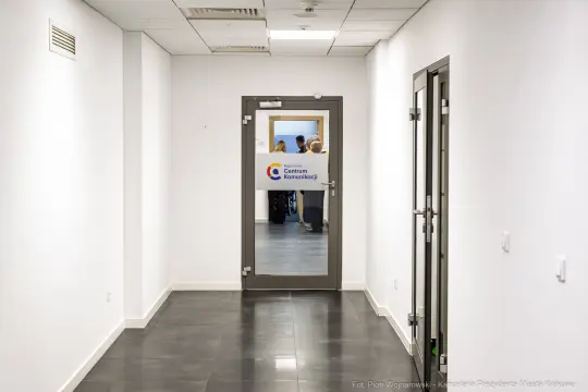 Korytarz z drzwiami do Centrum Komunikacji, w tle widoczni ludzie.