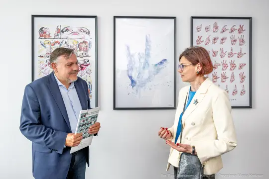 Mężczyzna i kobieta rozmawiają w pomieszczeniu z obrazami na ścianach.