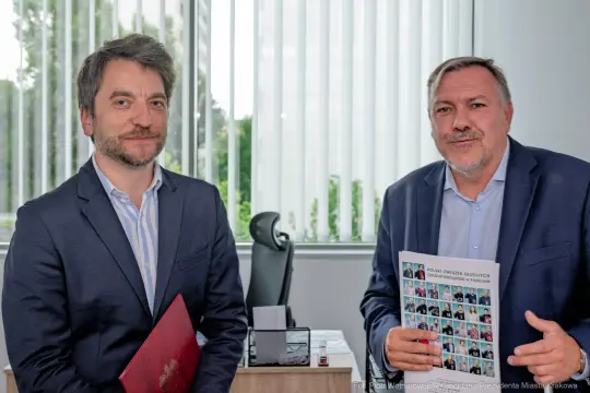 Dwóch mężczyzn w garniturach trzymających dokumenty w biurze.