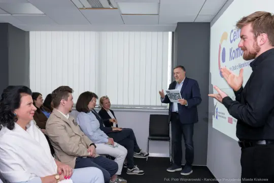 Spotkanie grupy ludzi z mężczyzną prezentującym informacje na ekranie.