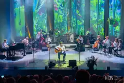Koncert z muzykami na scenie, różnorodne instrumenty, kolorowe tło.