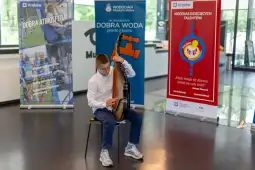 Chłopiec gra na instrumencie muzycznym w otoczeniu banerów promujących wydarzenia.
