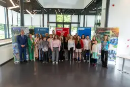 Grupa dzieci i dorosłych stoi przed banerami promocyjnymi w nowoczesnym wnętrzu.