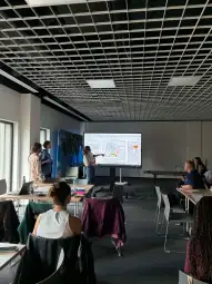 Prezentacja na dużym ekranie w sali konferencyjnej z uczestnikami dyskusji.