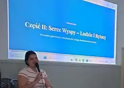 Kobieta mówi do mikrofonu, w tle slajd z tytułem o mieszkańcach i tradycjach wyspy.