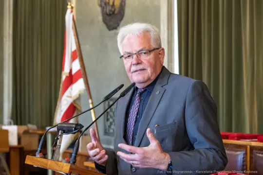 Mężczyzna w okularach przemawia przy mównicy w sali konferencyjnej.