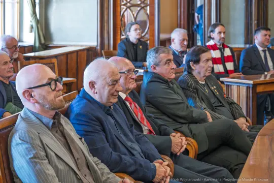 Grupa mężczyzn w eleganckich strojach siedzących w sali obrad.