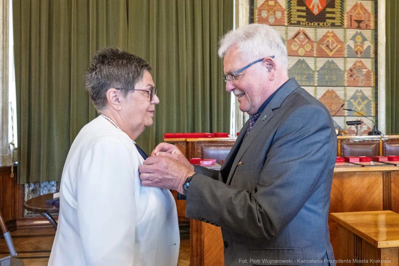 Uroczystość wręczenia odznaczenia. Mężczyzna przypina medal kobiecie.  Autor: Piotr Wojnarowski