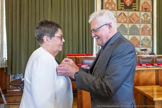 Uroczystość wręczenia odznaczenia. Mężczyzna przypina medal kobiecie.