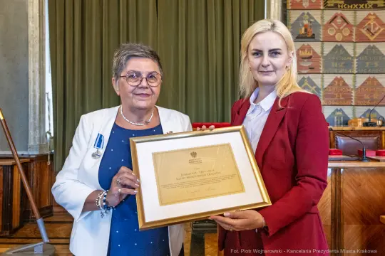 Kobiety trzymające dyplom w sali z dekoracjami.