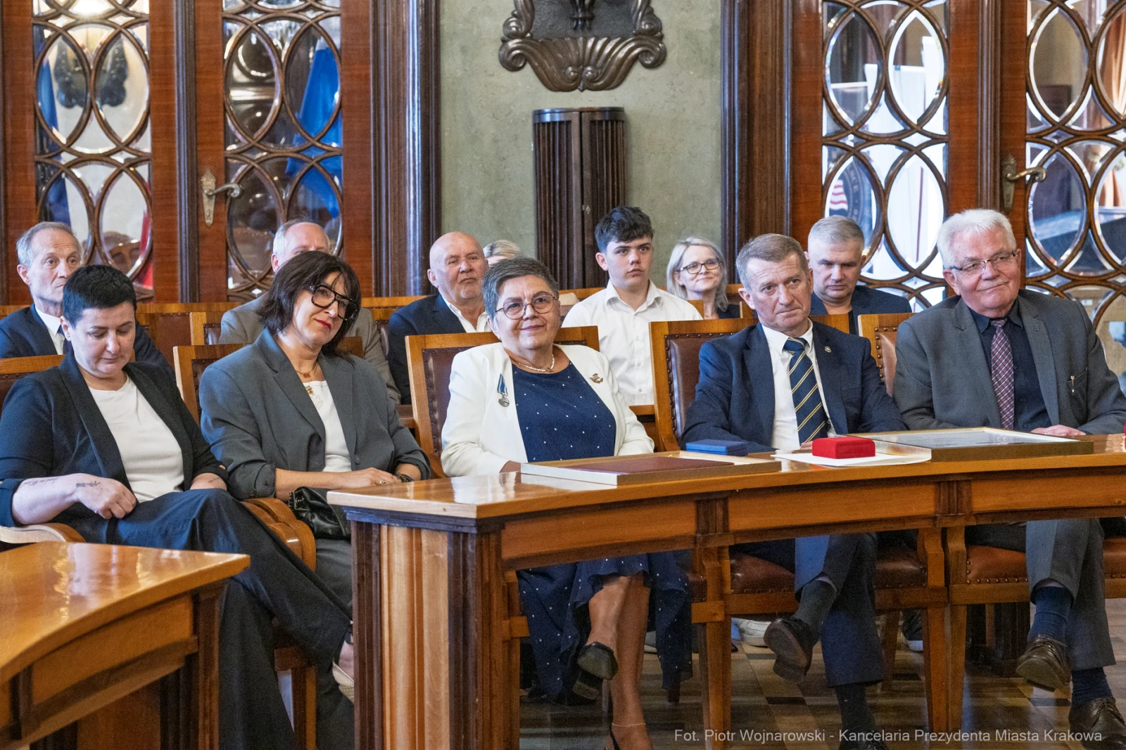 Grupa osób siedzących w sali, w tle dekoracyjne okna i stoły.  Autor: Piotr Wojnarowski
