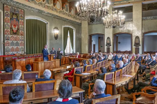 Spotkanie w sali obrad z mówcą i słuchaczami w historycznym wnętrzu.
