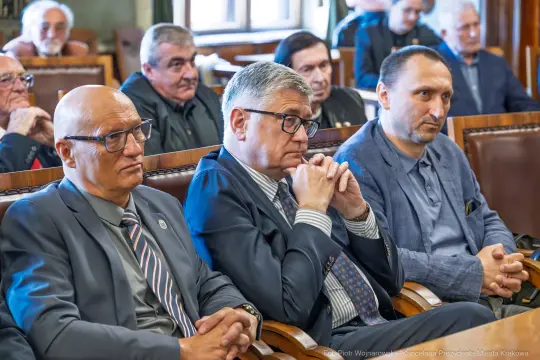 Grupa mężczyzn w garniturach siedzących w sali obrad, skupionych na dyskusji.