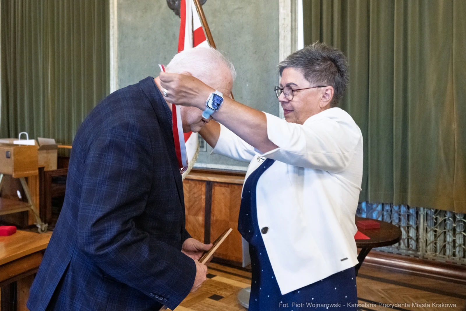 Wręczenie odznaczenia przez kobietę mężczyźnie w formalnym otoczeniu.  Autor: Piotr Wojnarowski