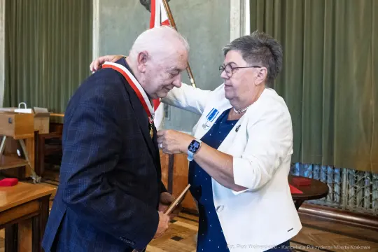 Mężczyzna otrzymuje medal od kobiety w białym żakiecie.