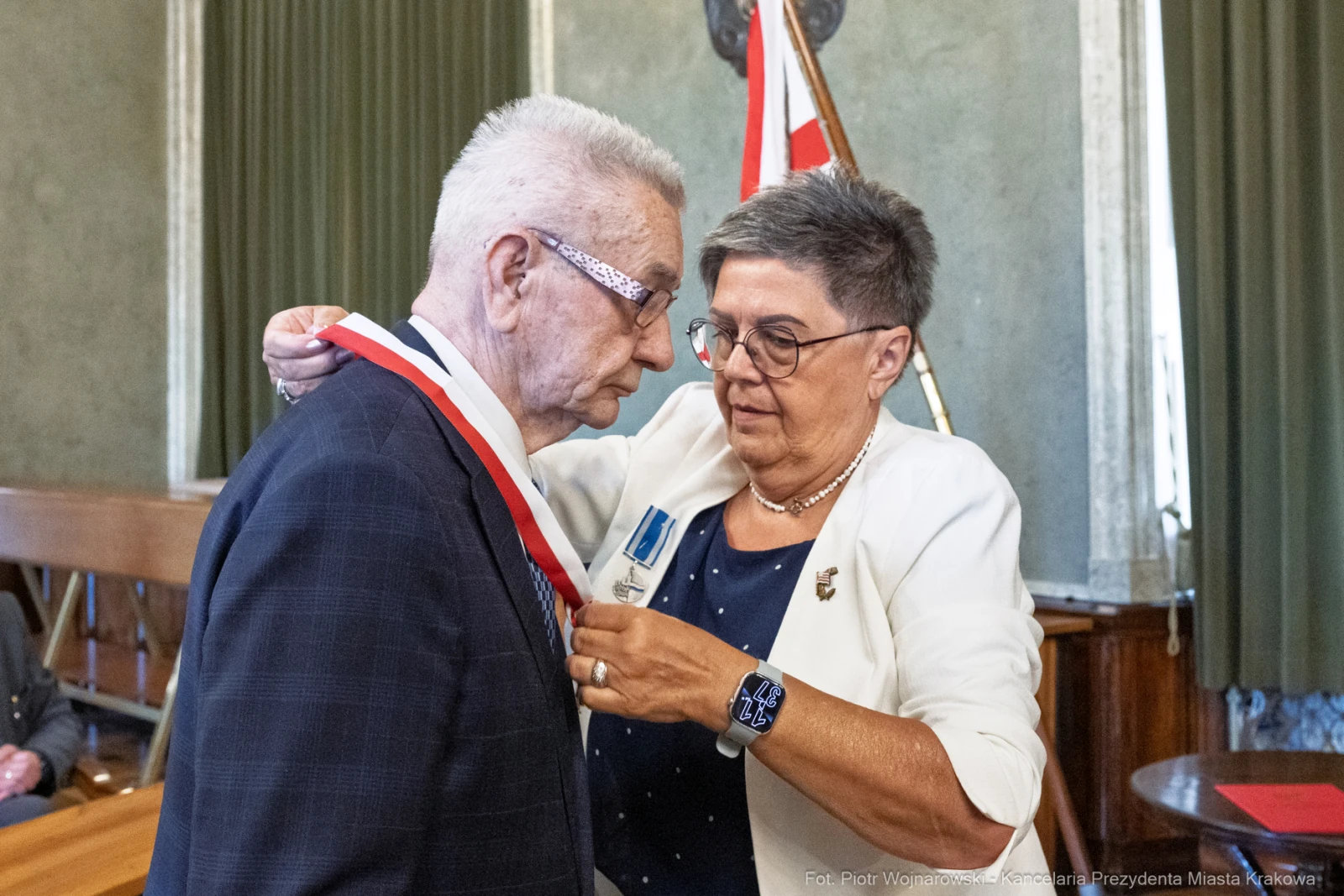 Mężczyzna otrzymuje medal od kobiety w formalnym otoczeniu.  Autor: Piotr Wojnarowski