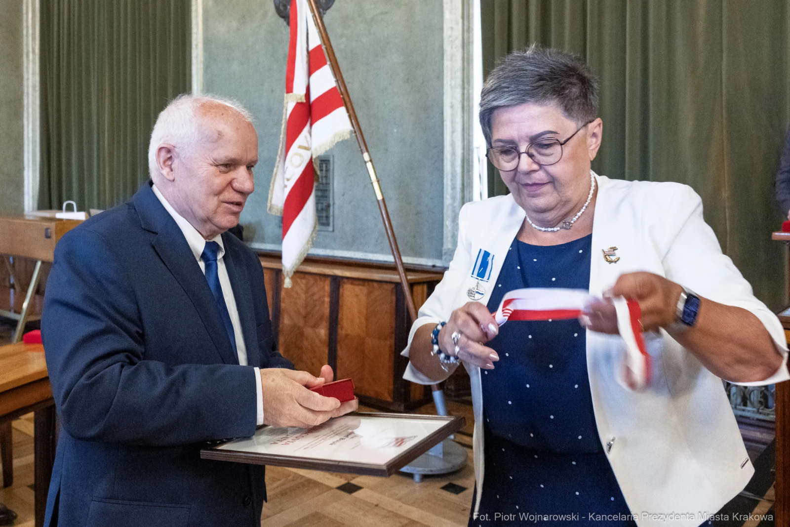 Wręczenie odznaczenia przez mężczyznę kobiecie w oficjalnym otoczeniu.  Autor: Piotr Wojnarowski
