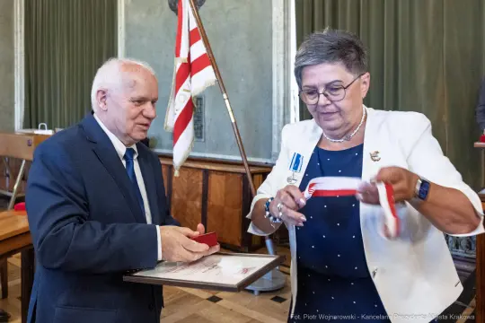 Wręczenie odznaczenia przez mężczyznę kobiecie w oficjalnym otoczeniu.