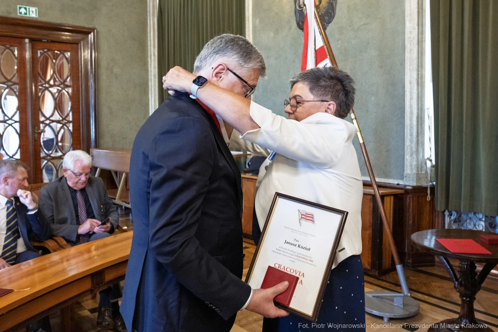Wręczenie nagrody przez kobietę mężczyźnie w sali z flagą i dokumentami.  Autor: Piotr Wojnarowski