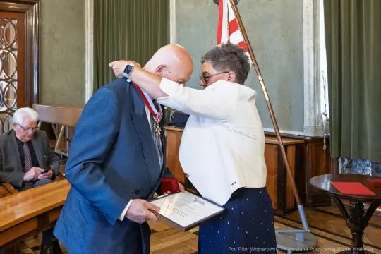 Wręczenie odznaczenia przez kobietę mężczyźnie w formalnym otoczeniu.