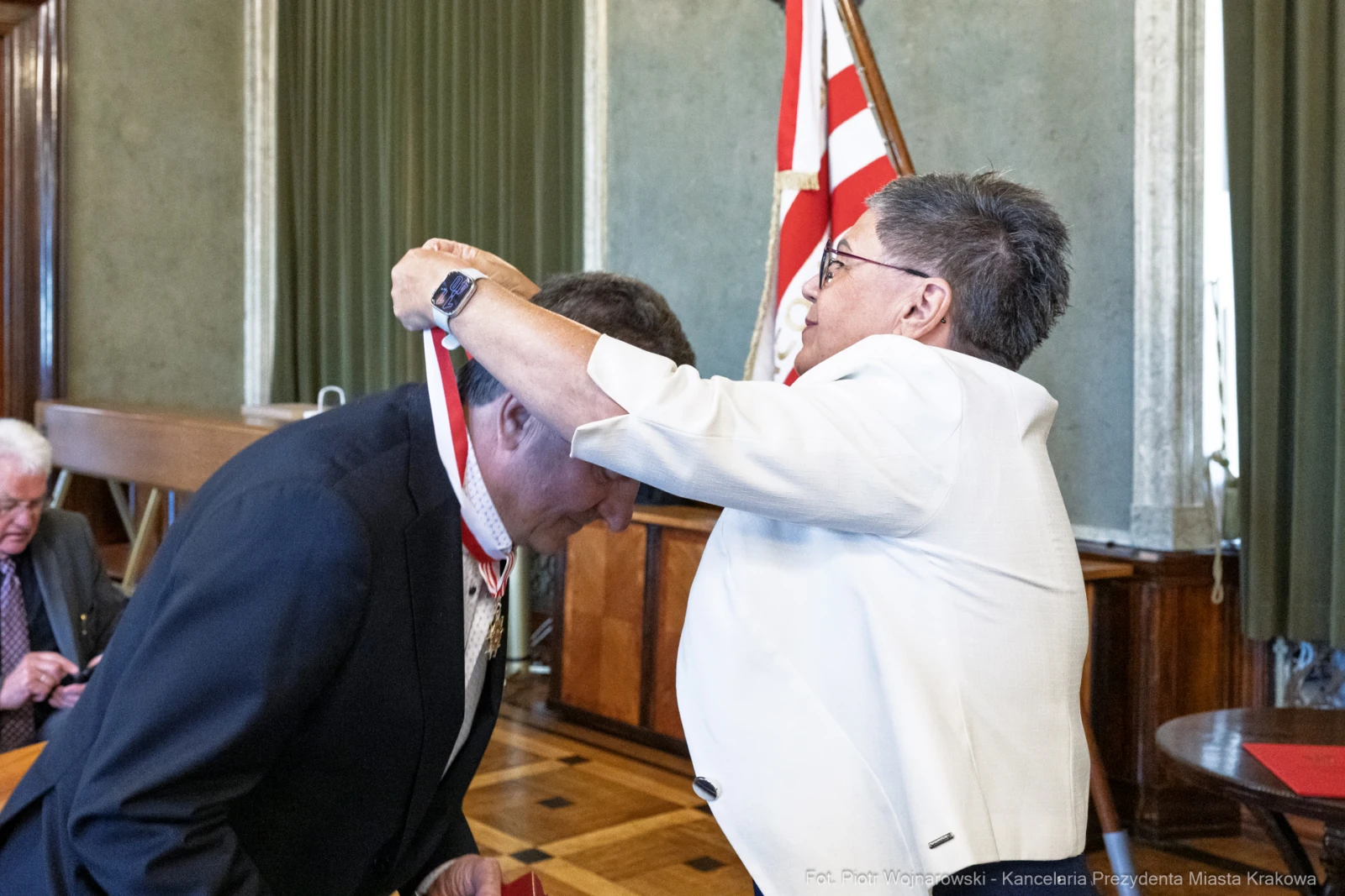 Wręczenie odznaczenia przez kobietę mężczyźnie w formalnym otoczeniu.  Autor: Piotr Wojnarowski