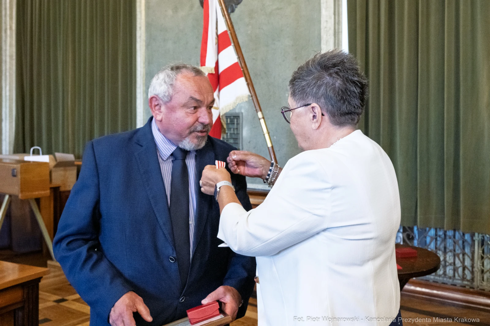 Mężczyzna odbiera medal od kobiety w oficjalnym otoczeniu.  Autor: Piotr Wojnarowski
