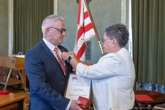 Wręczenie odznaczenia przez kobietę mężczyźnie w formalnym stroju.