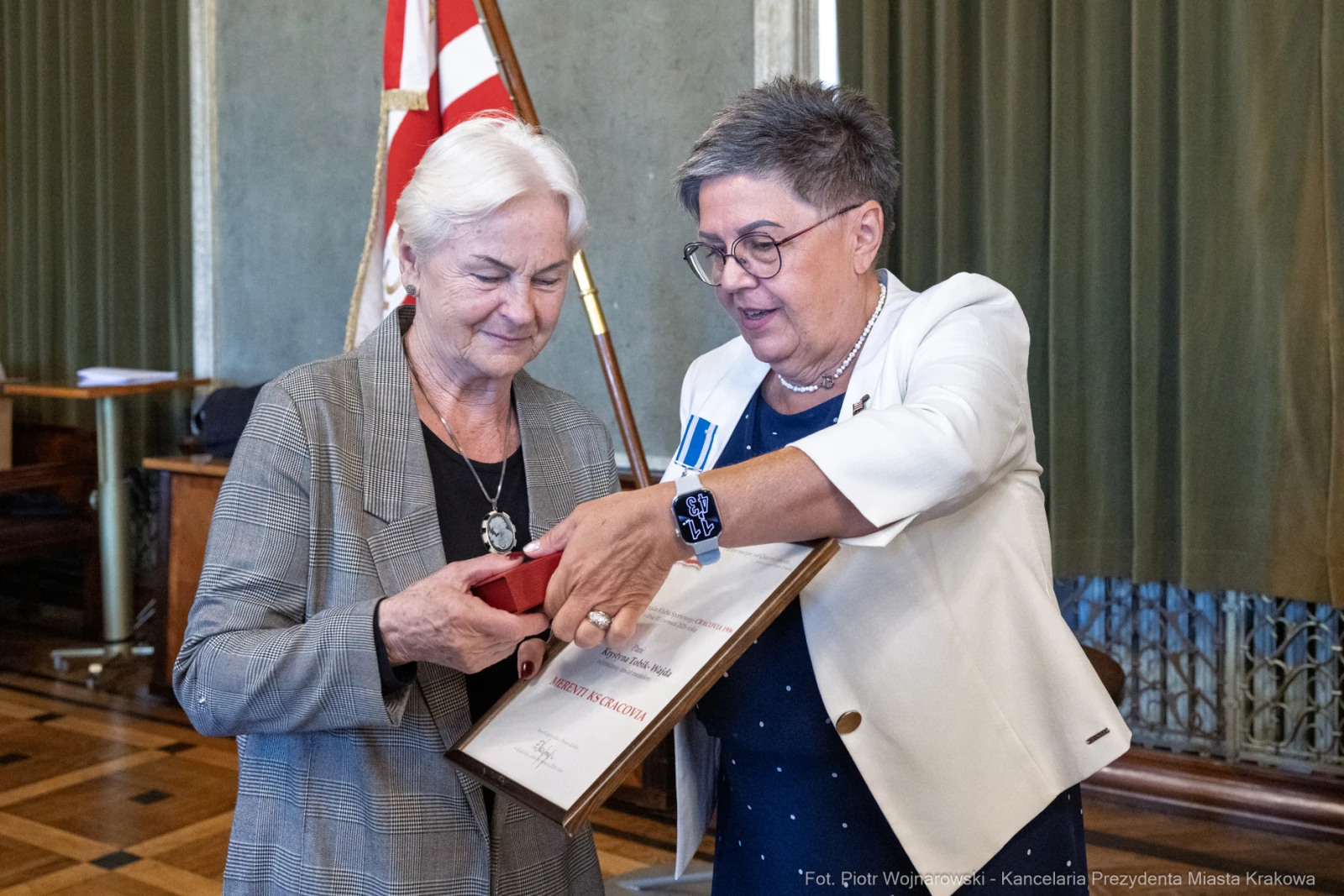 Wręczenie odznaczenia przez kobietę w okularach drugiej kobiecie z białymi włosami.  Autor: Piotr Wojnarowski