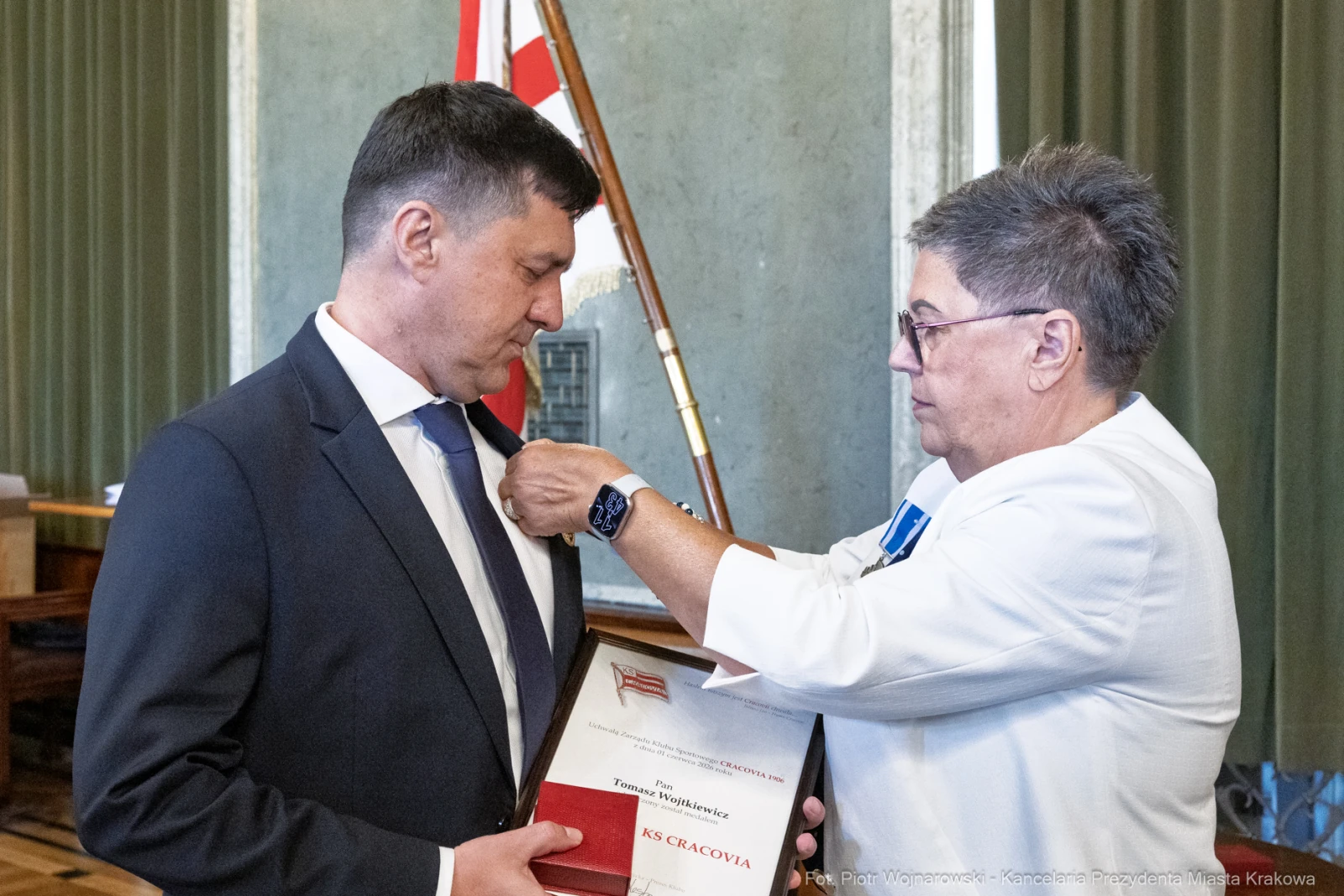 Wręczenie odznaczenia przez kobietę mężczyźnie w formalnym otoczeniu.  Autor: Piotr Wojnarowski