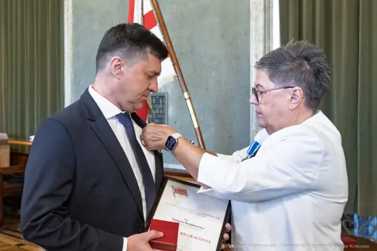 Wręczenie odznaczenia przez kobietę mężczyźnie w formalnym otoczeniu.