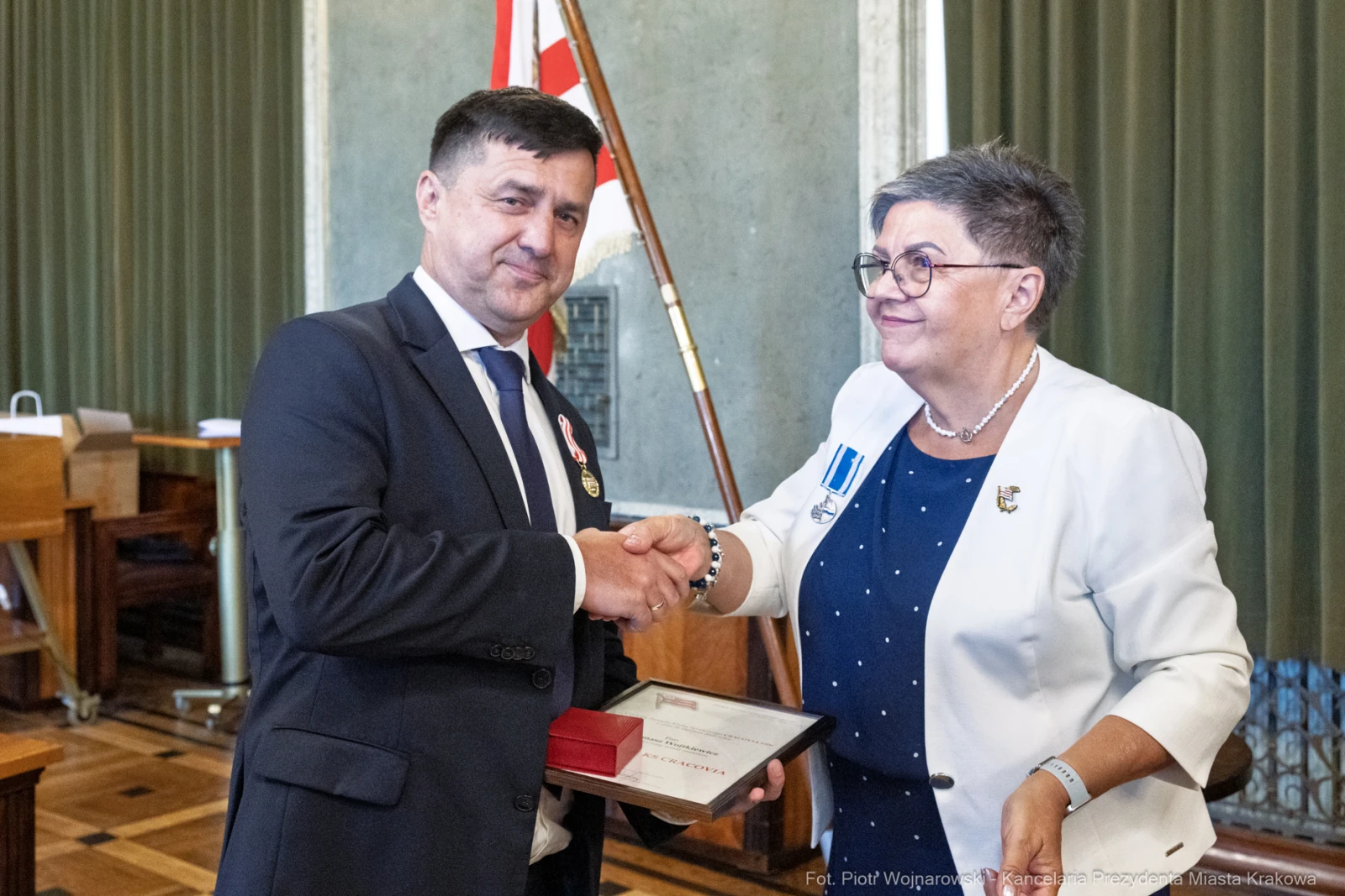 Mężczyzna odbierający medal od kobiety w formalnym otoczeniu.  Autor: Piotr Wojnarowski