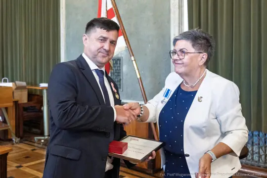 Mężczyzna odbierający medal od kobiety w formalnym otoczeniu.