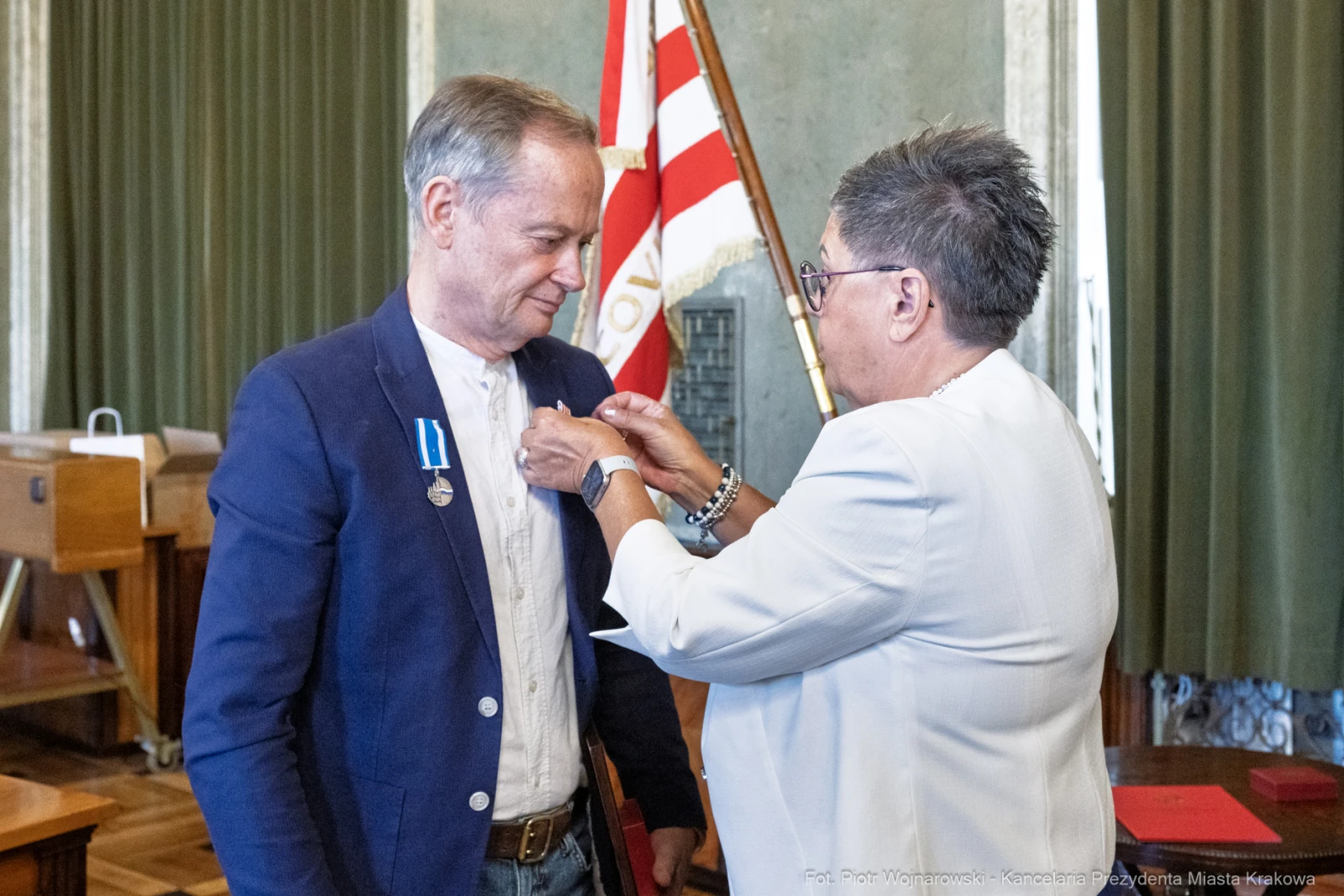 Mężczyzna otrzymuje medal od kobiety w urzędzie, w tle flagi.  Autor: Piotr Wojnarowski