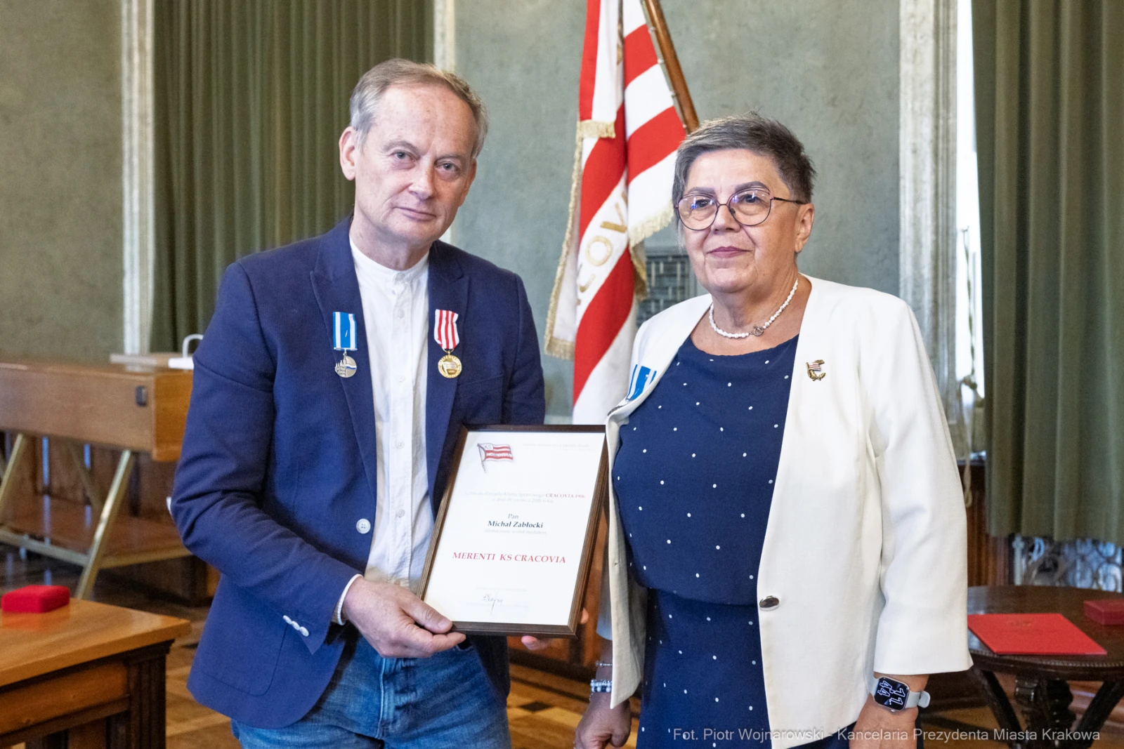 Mężczyzna i kobieta z medalami, wręczający sobie dyplom w sali z flagą.  Autor: Piotr Wojnarowski
