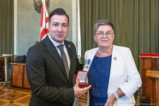 Wręczenie medalu przez mężczyznę kobiecie w oficjalnym otoczeniu.