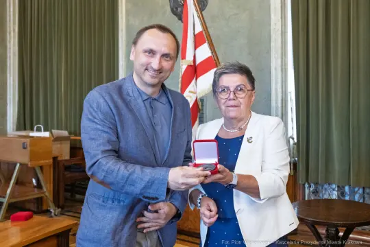 Mężczyzna i kobieta trzymają medal w eleganckim pomieszczeniu.