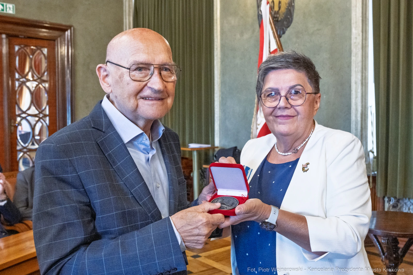 Mężczyzna i kobieta wręczają sobie medal w uroczystym otoczeniu.  Autor: Piotr Wojnarowski