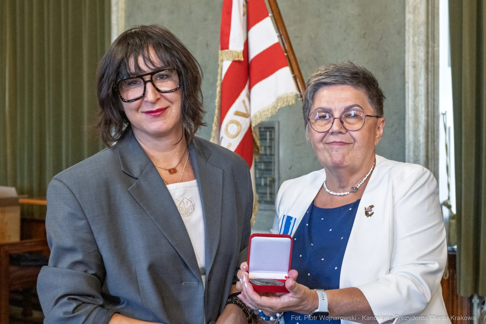 Dwie kobiety trzymają medal w eleganckim pudełku, w tle flaga.  Autor: Piotr Wojnarowski
