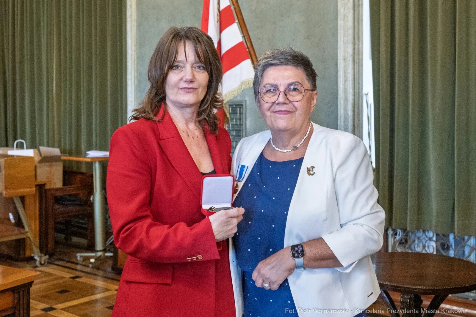 Wręczenie odznaczenia przez jedną kobietę drugiej w eleganckim otoczeniu.  Autor: Piotr Wojnarowski