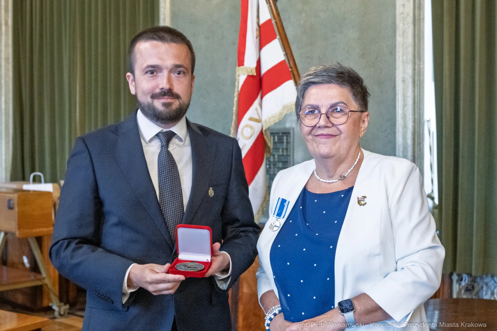 Mężczyzna wręcza medal kobiecie w eleganckich strojach, w tle flagi.  Autor: Piotr Wojnarowski