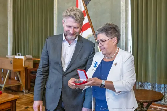 Wręczenie medalu przez kobietę w okularach mężczyźnie w garniturze.
