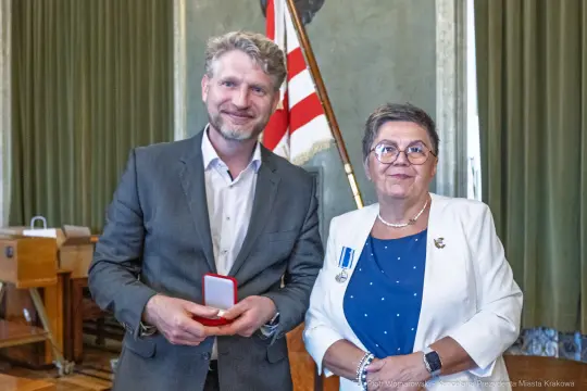 Mężczyzna i kobieta z medalem w sali z flagą.