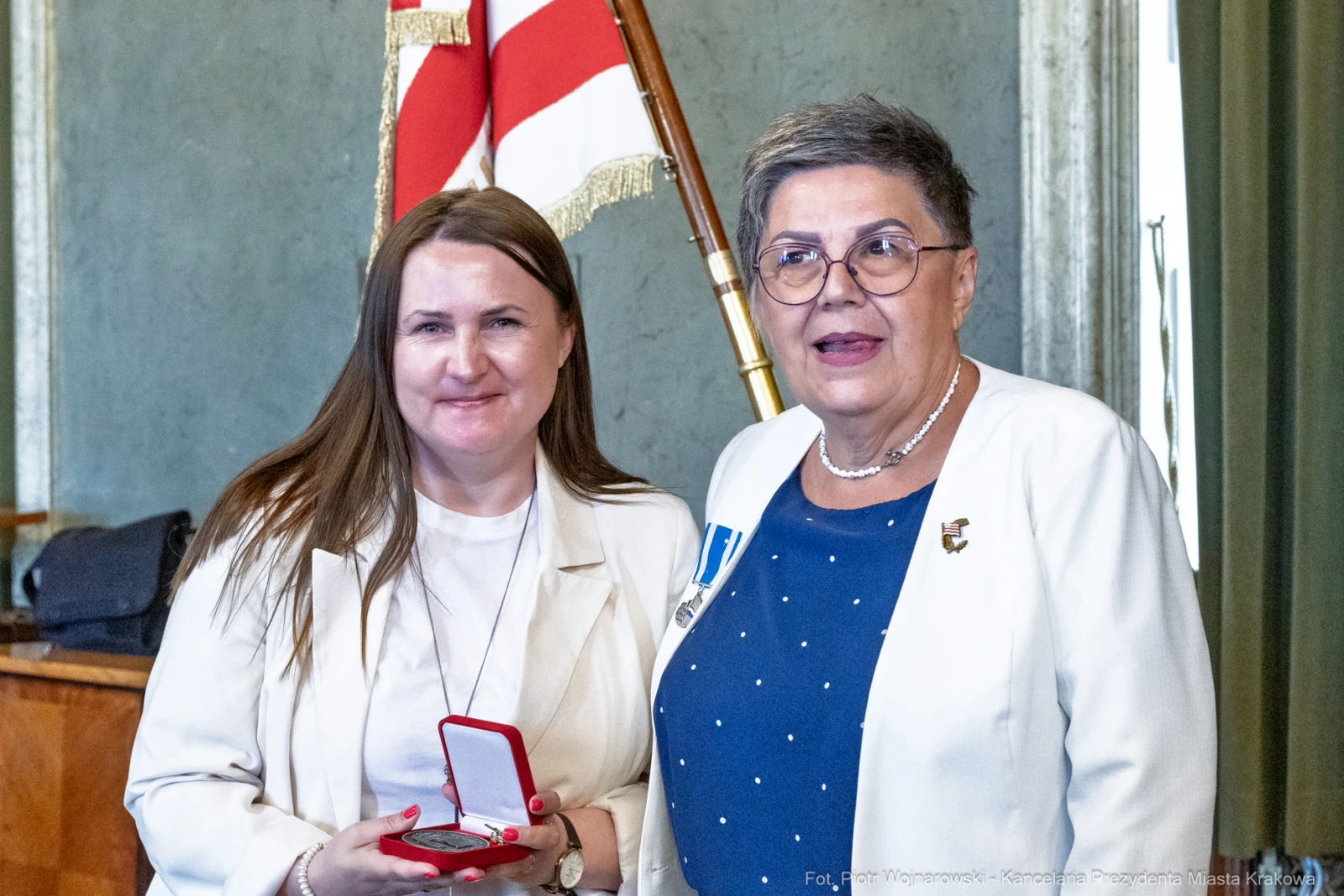 Dwie kobiety w eleganckich strojach, jedna z medalem w dłoni, w tle flagi.  Autor: Piotr Wojnarowski