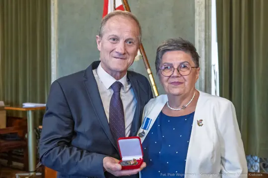 Mężczyzna i kobieta trzymają medal w eleganckim otoczeniu.