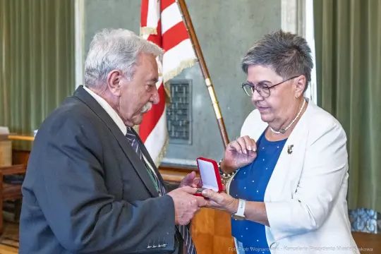 Wręczenie odznaczenia przez kobietę mężczyźnie w formalnym otoczeniu.