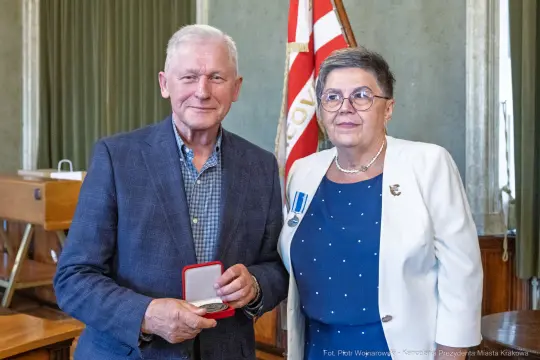 Mężczyzna i kobieta z medalem w sali z flagą.