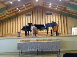 Dwoje muzyków grających na wiolonczelach z fortepianem w tle.