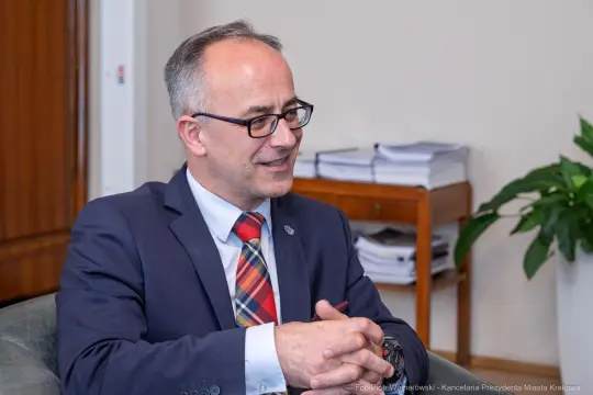 Mężczyzna w okularach, w garniturze, rozmawia w biurze.