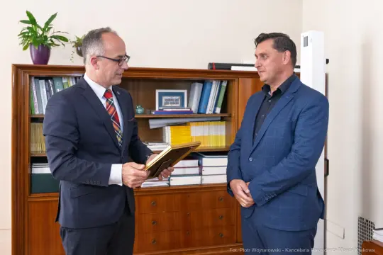 Mężczyzna wręcza dyplom drugiemu mężczyźnie w biurze.