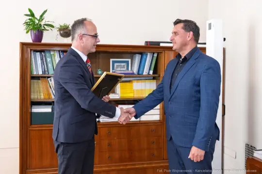 Dwaj mężczyźni uścisnęli sobie dłonie, jeden z nich trzyma dokumenty.